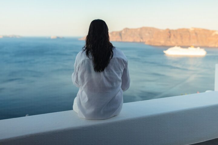 Woman sitting on a ship deck looking out over the sea toward a coastline
