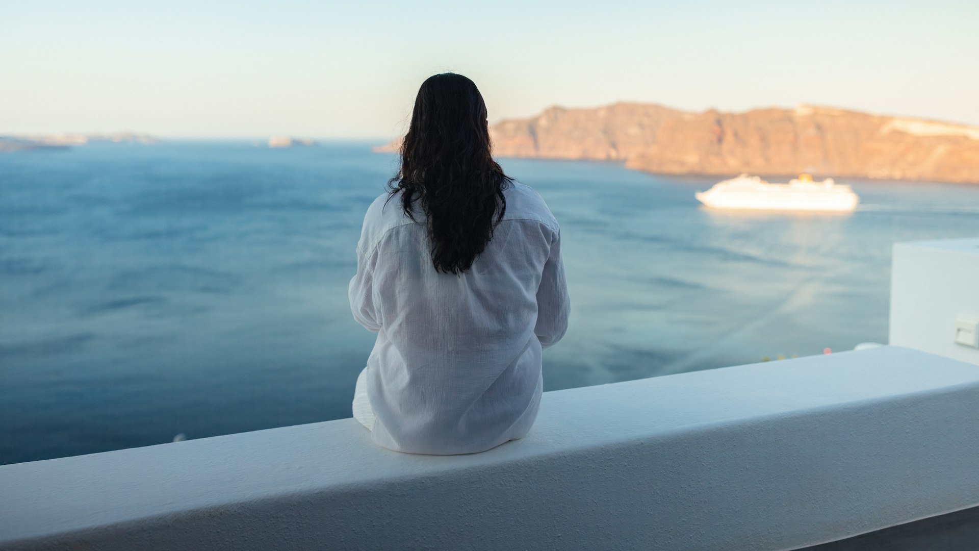 Woman sitting on a ship deck looking out over the sea toward a coastline