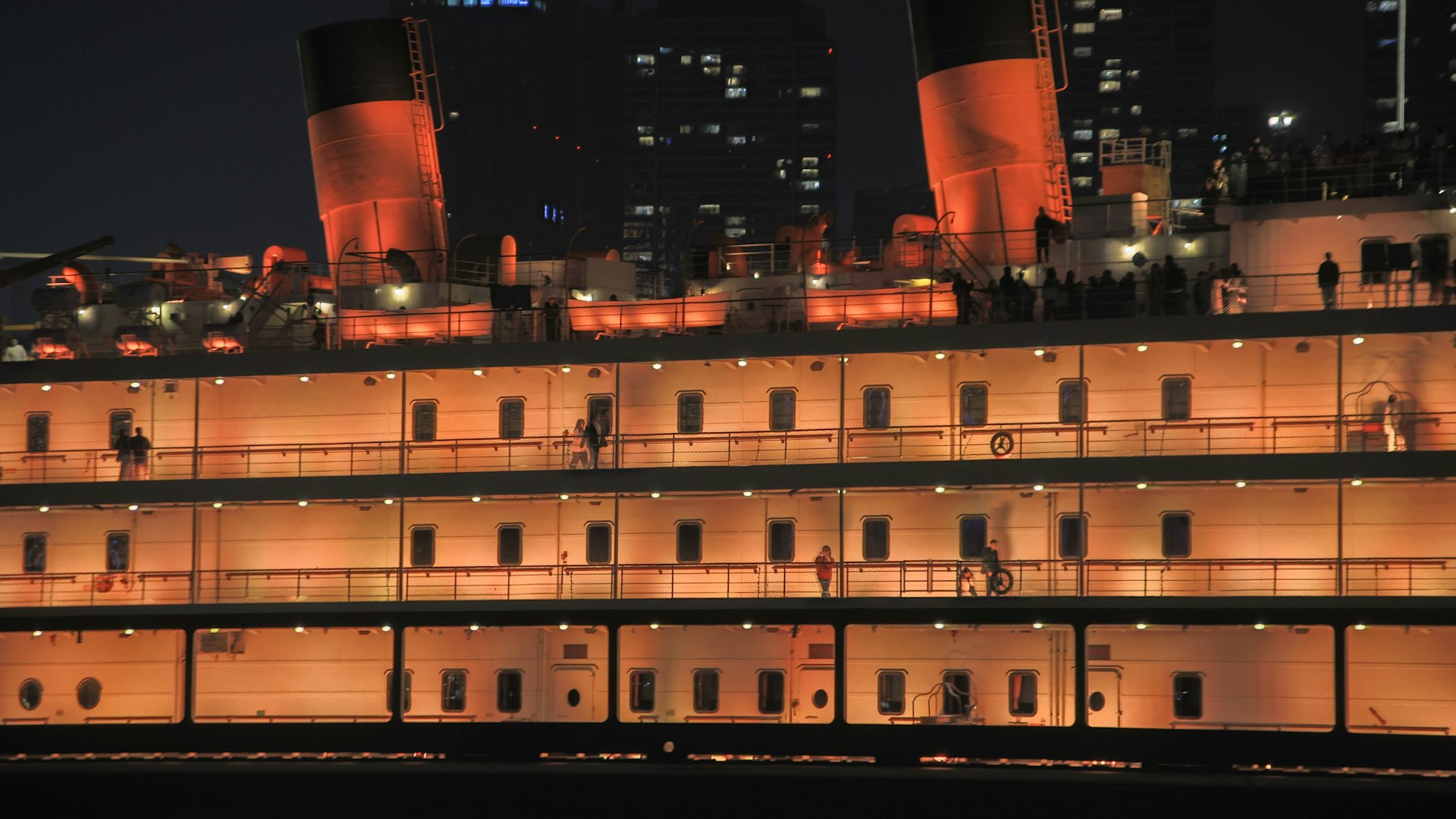 The Queen Mary ocean liner lit up at night with its red funnels