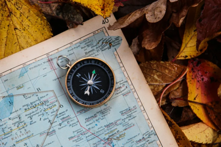 Compass lying on an old map among autumn leaves
