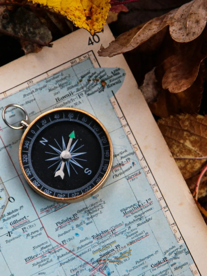 Compass lying on an old map among autumn leaves