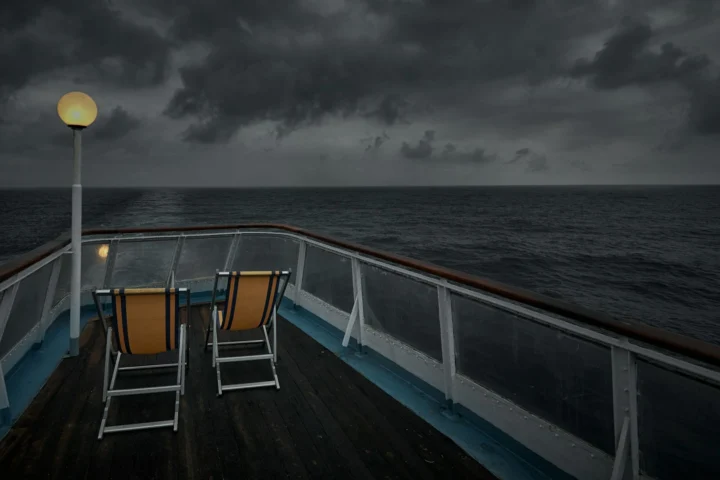 Two deck chairs on the bow of a ship under a stormy sky