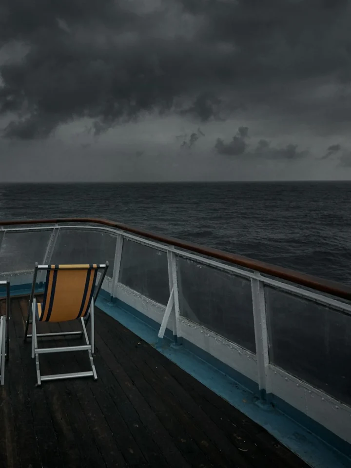 Two deck chairs on the bow of a ship under a stormy sky